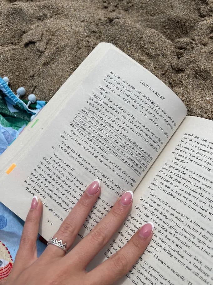 An open novel on the sand, next to a hand.