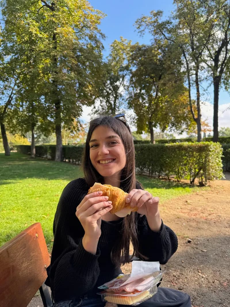 Pili smiling with a croissant in a park.